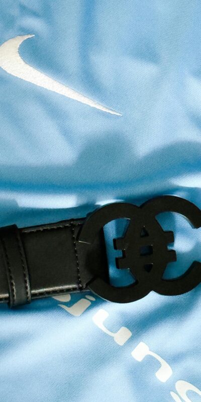 Close-up of a luxurious black leather belt with unique buckle on a blue fabric background.