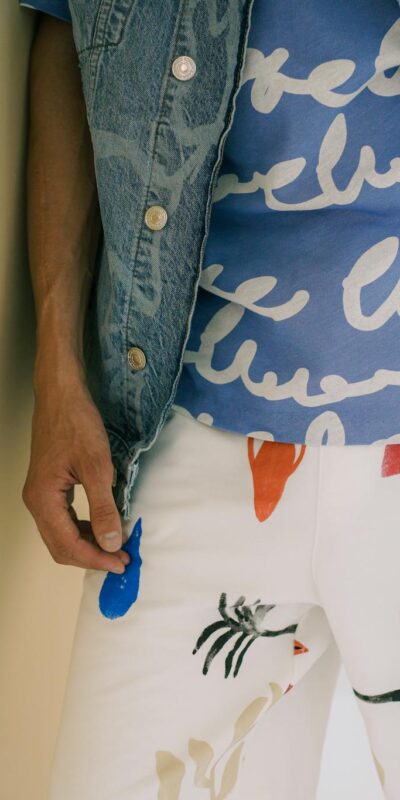 Close-up of a stylish outfit featuring a denim vest, blue graphic t-shirt, and patterned white pants.