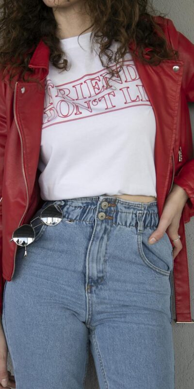 Fashionable woman in red jacket and jeans posing against a gray wall, showcasing casual style.