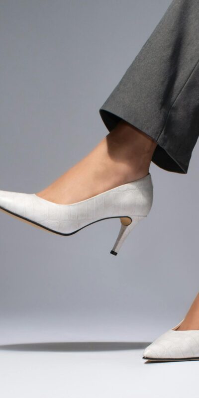 Stylish white heels paired with gray trousers showcased in a studio setting.