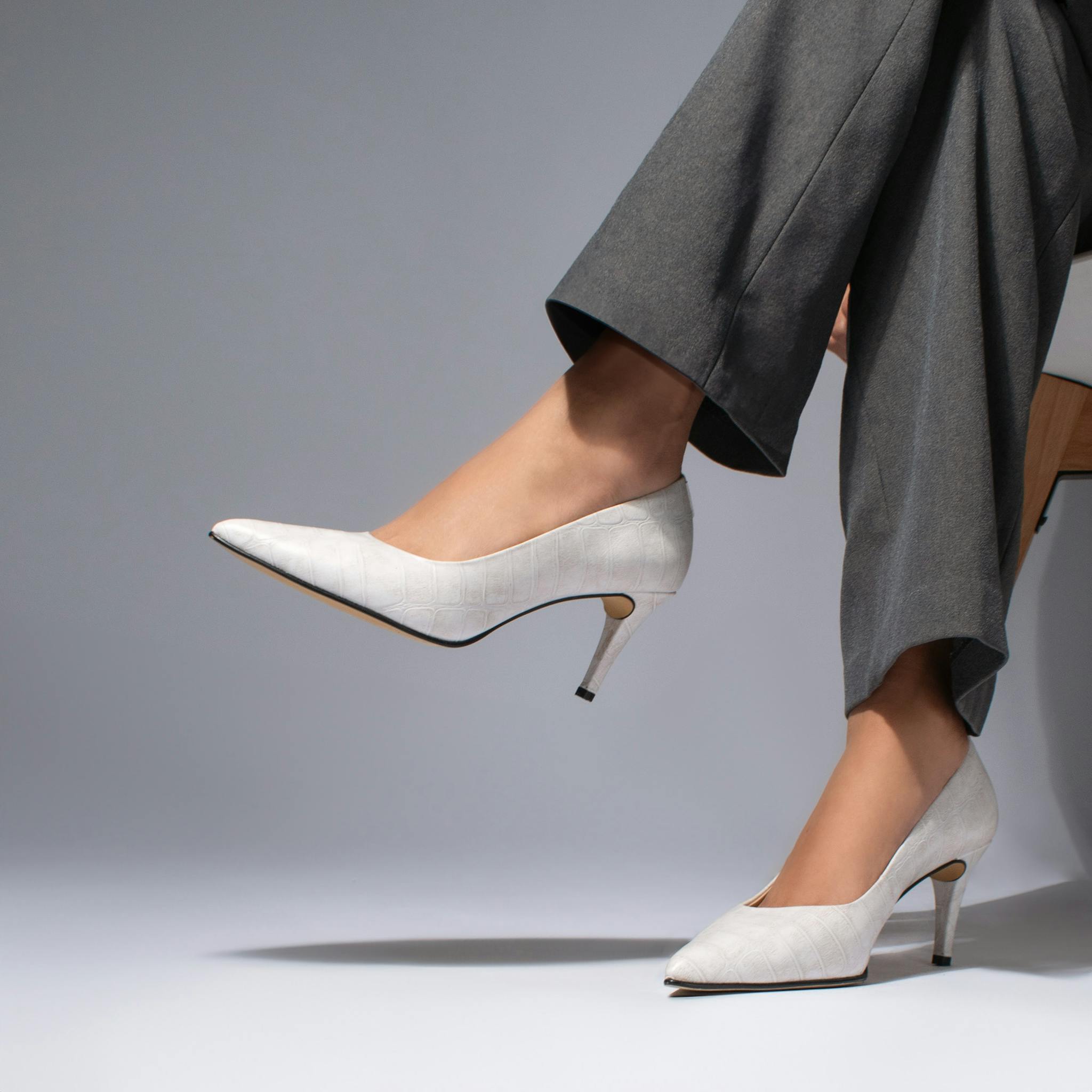 Stylish white heels paired with gray trousers showcased in a studio setting.